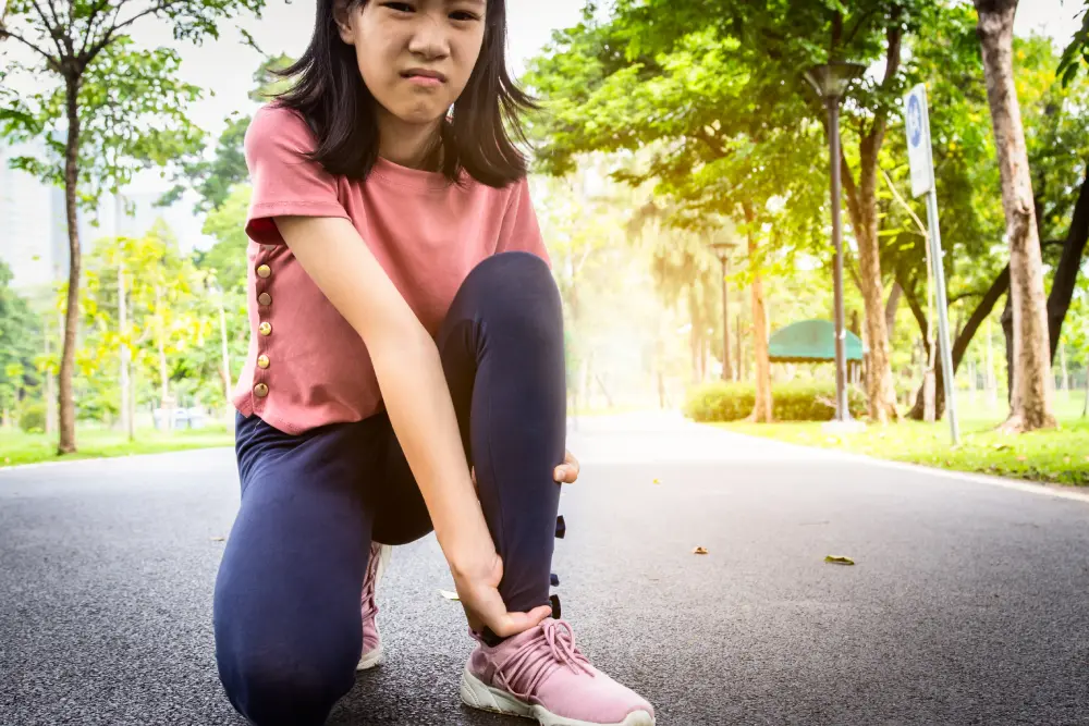 A girl holding her injured ankle in a park.