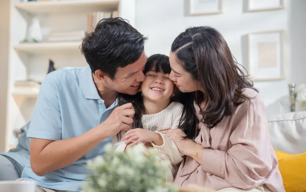 Parents kissing their smiling daughter on the cheeks.