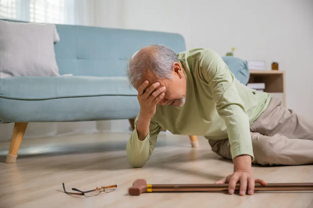 An elderly man lying on the floor holding his head.